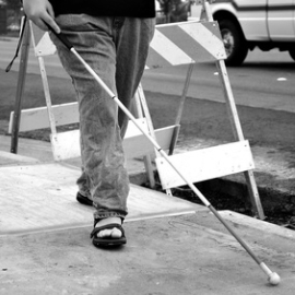 Foto von einem blinden Mann mit Langstock, eine provisorische und gefhrliche Baustellenabdeckung berquerend